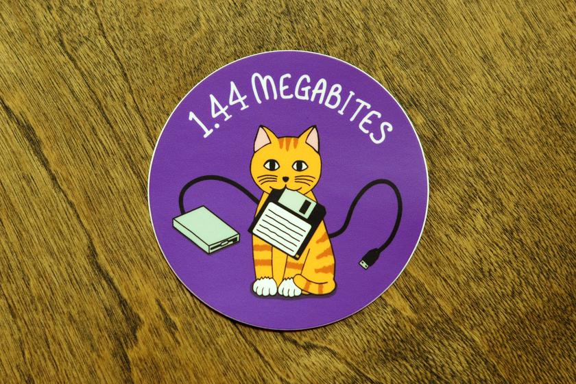 Vinyl sticker with smiling orange tabby kitty sitting holding a floppy disk in its mouth.