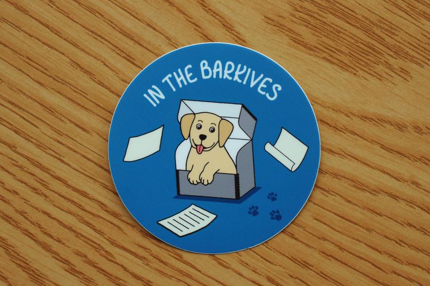 Vinyl sticker with smiling doggy sitting in an archival box with the lid open. The caption says In the barkives.